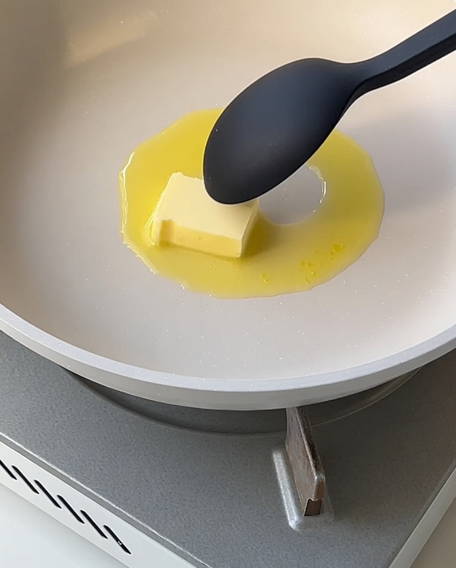 Una salsa bianca liscia che si addensa in padella, mescolata con un cucchiaio.