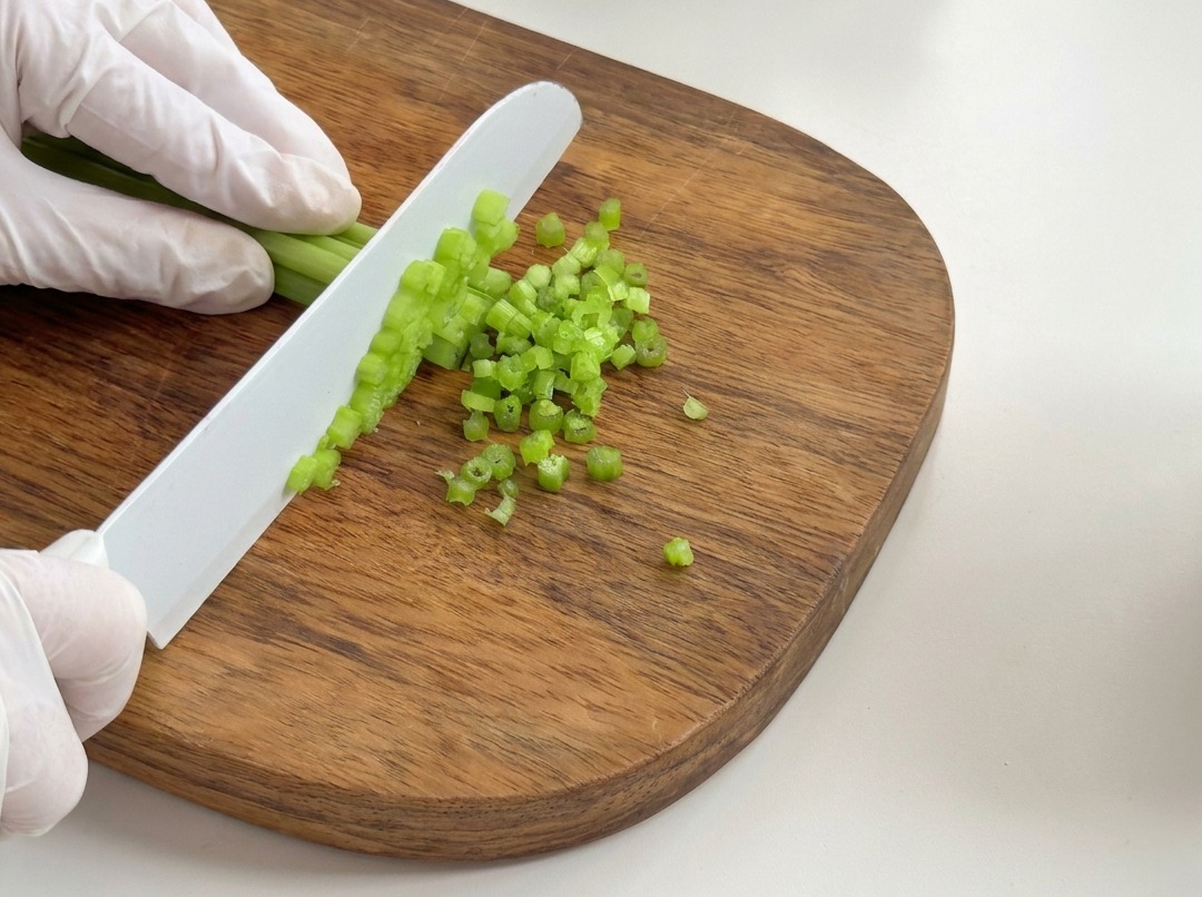 Gambi di sedano fresco tagliati a piccoli pezzetti su un tagliere.