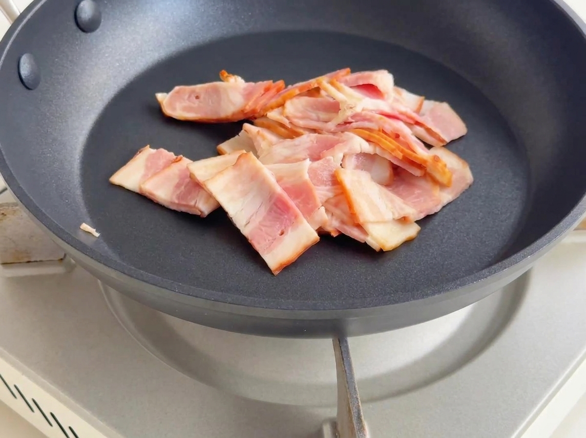Pezzetti di pancetta che friggono in padella, rilasciando il grasso e dorandosi.