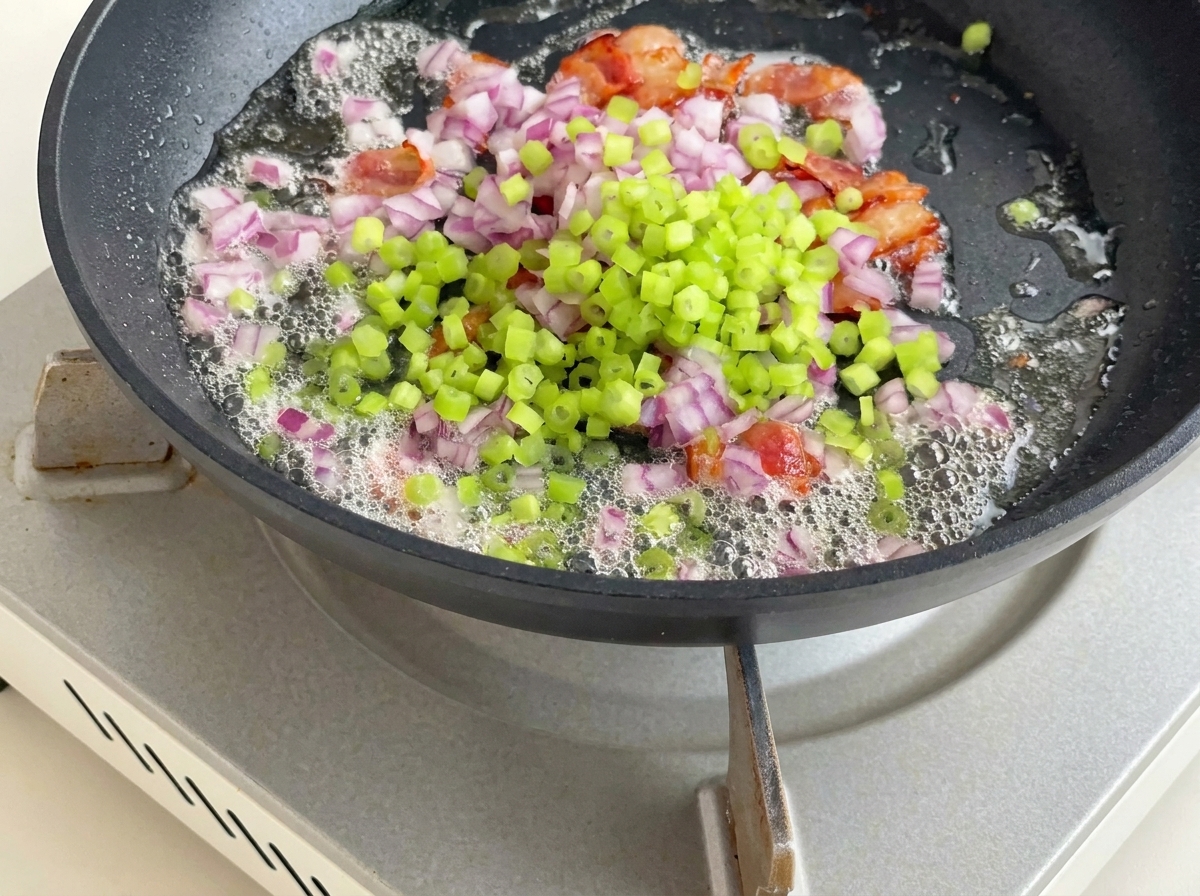 Patate a cubetti, sedano e cipolla rossa mescolati in padella con la pancetta e il suo grasso.