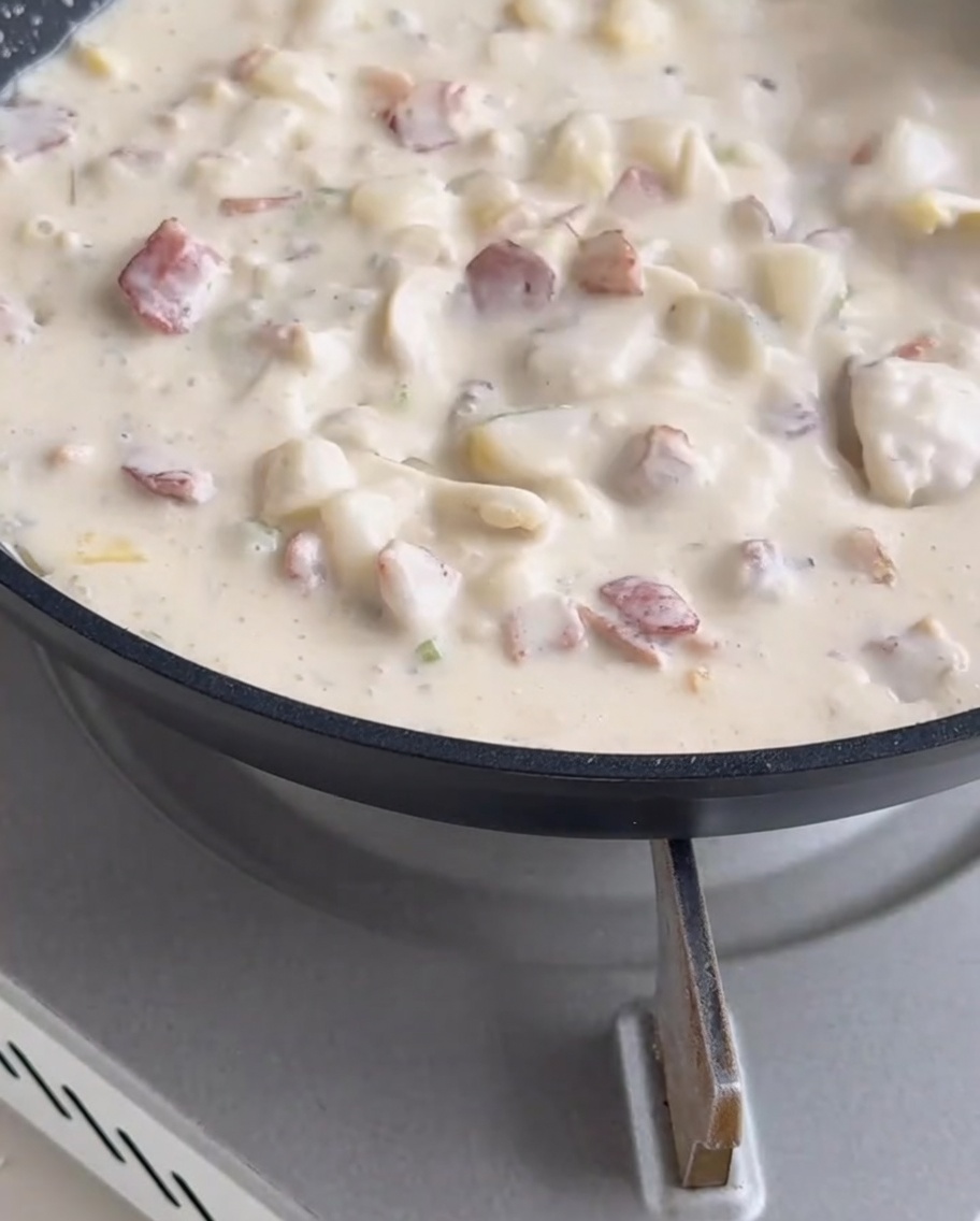 Molluschi mescolati allinterno della zuppa cremosa che bolle in padella.