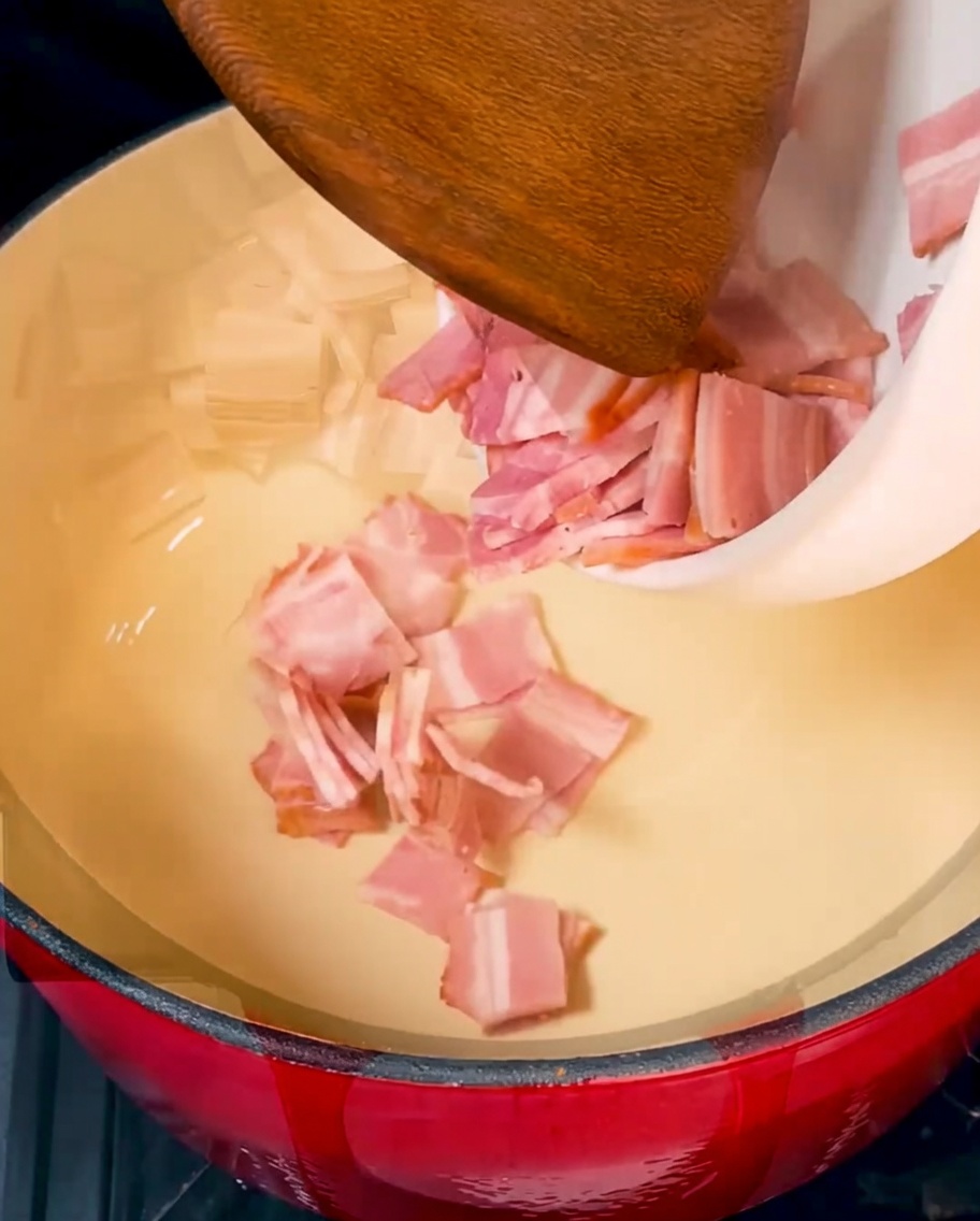 Pezzi di bacon croccanti e dorati che sfrigolano in una pentola di ghisa rossa.