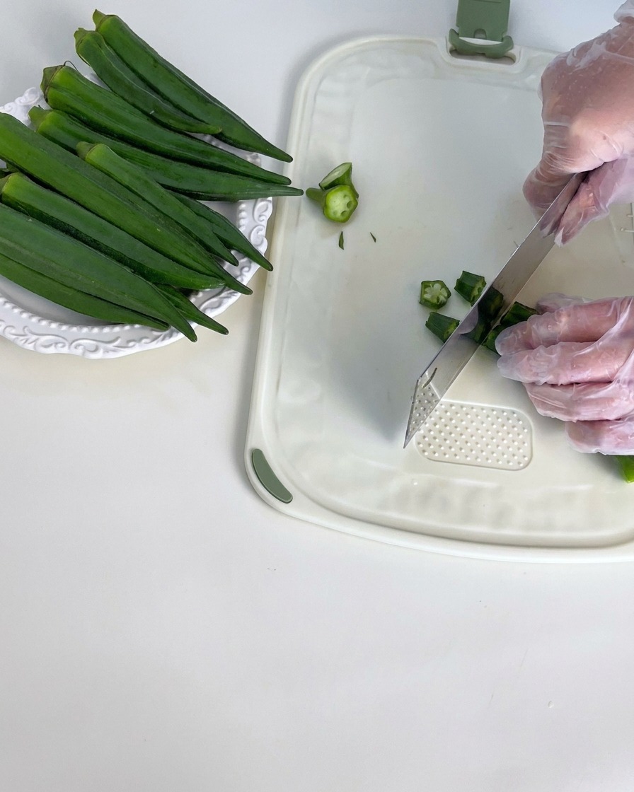 Baccelli di okra verde fresca tagliati su un tagliere bianco.