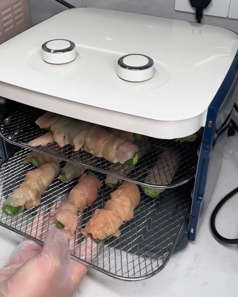 Griglie metalliche con involtini di pollo inserite in un essiccatore alimentare.