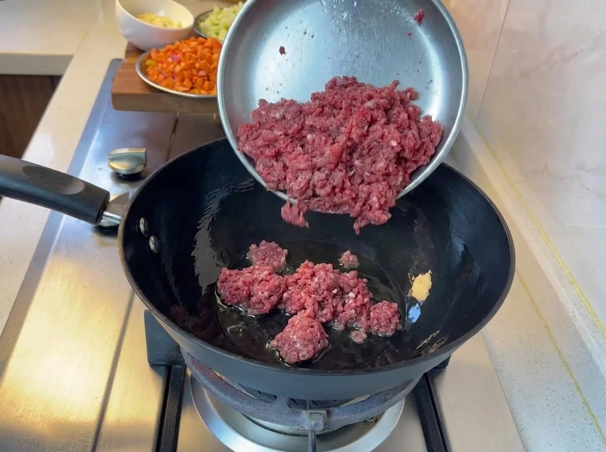 Carne macinata in cottura in una padella nera sui fornelli.