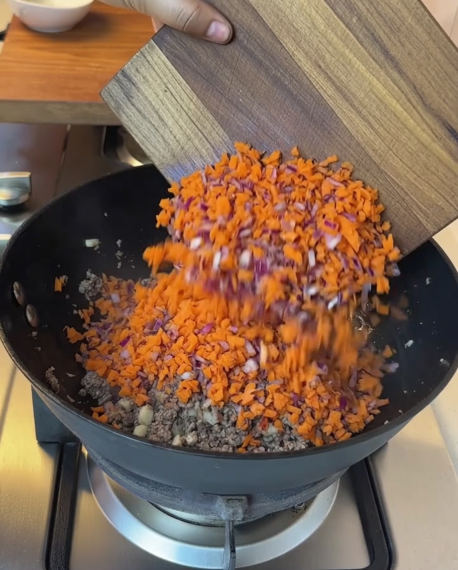 Verdure tritate e pomodori a cubetti aggiunti nella padella con la carne cotta.