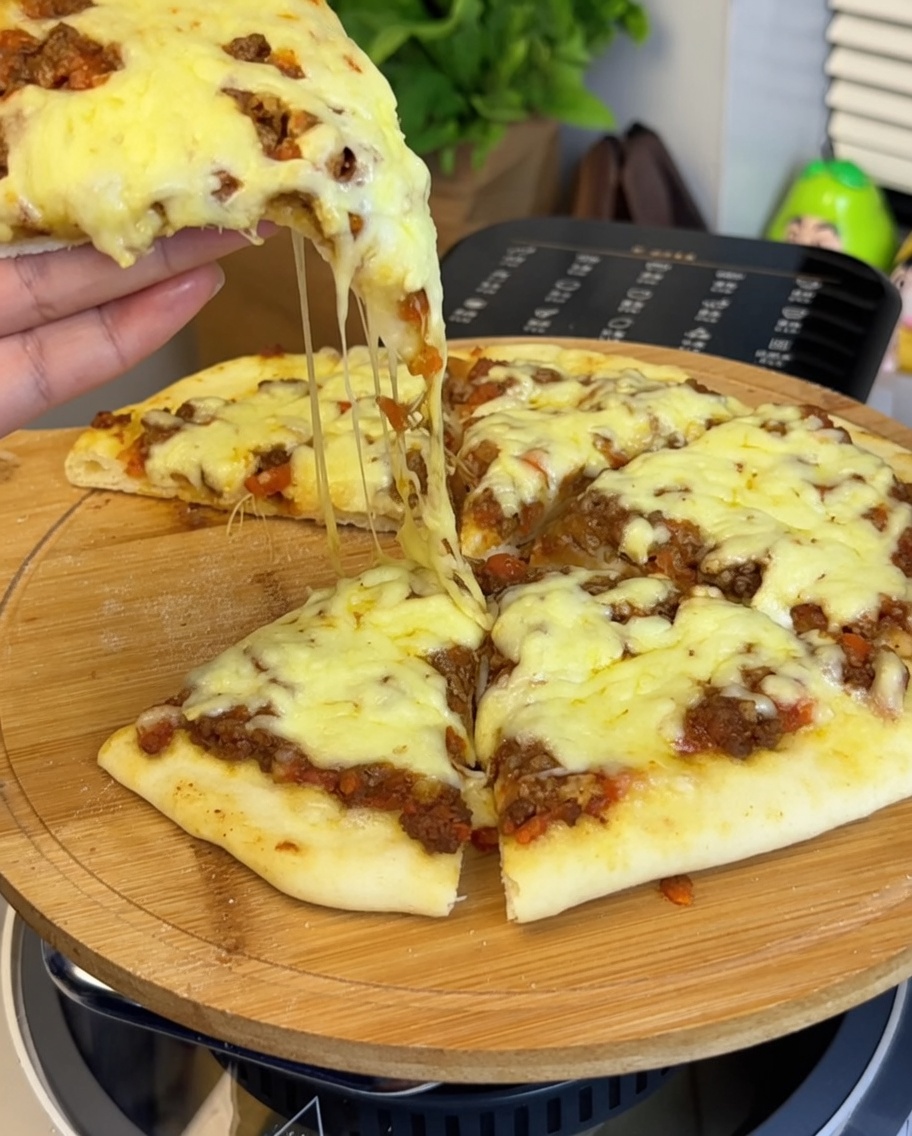 Primo piano del ragù di carne steso sulla base della pizza, con in primo piano una mano che tiene uno spicchio mostrando il formaggio filante.