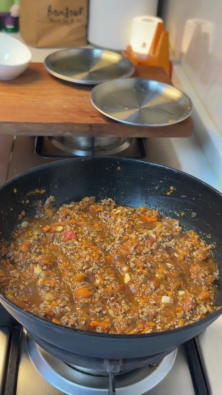 Una pizza appena sfornata con ricco sugo di carne e formaggio filante, servita su un tagliere rustico di legno.