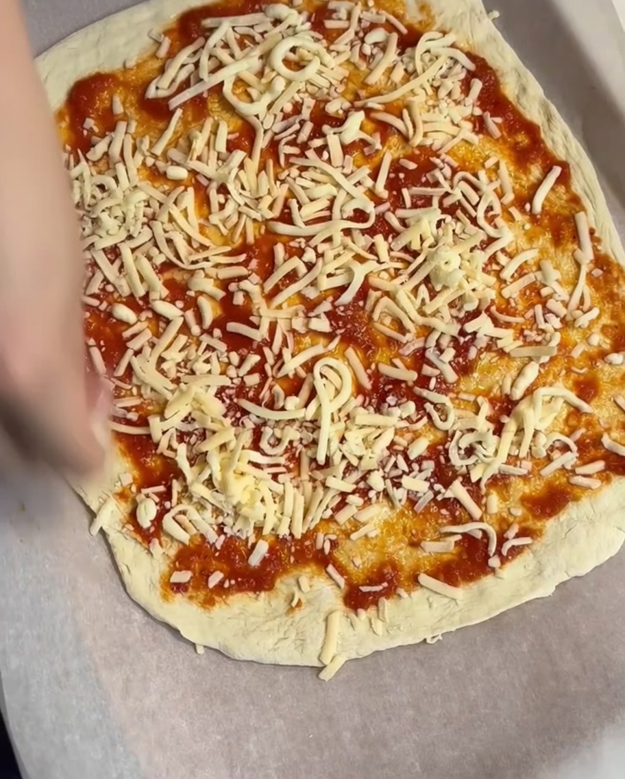 Uno strato di mozzarella grattugiata distribuito sopra la base di pomodoro.