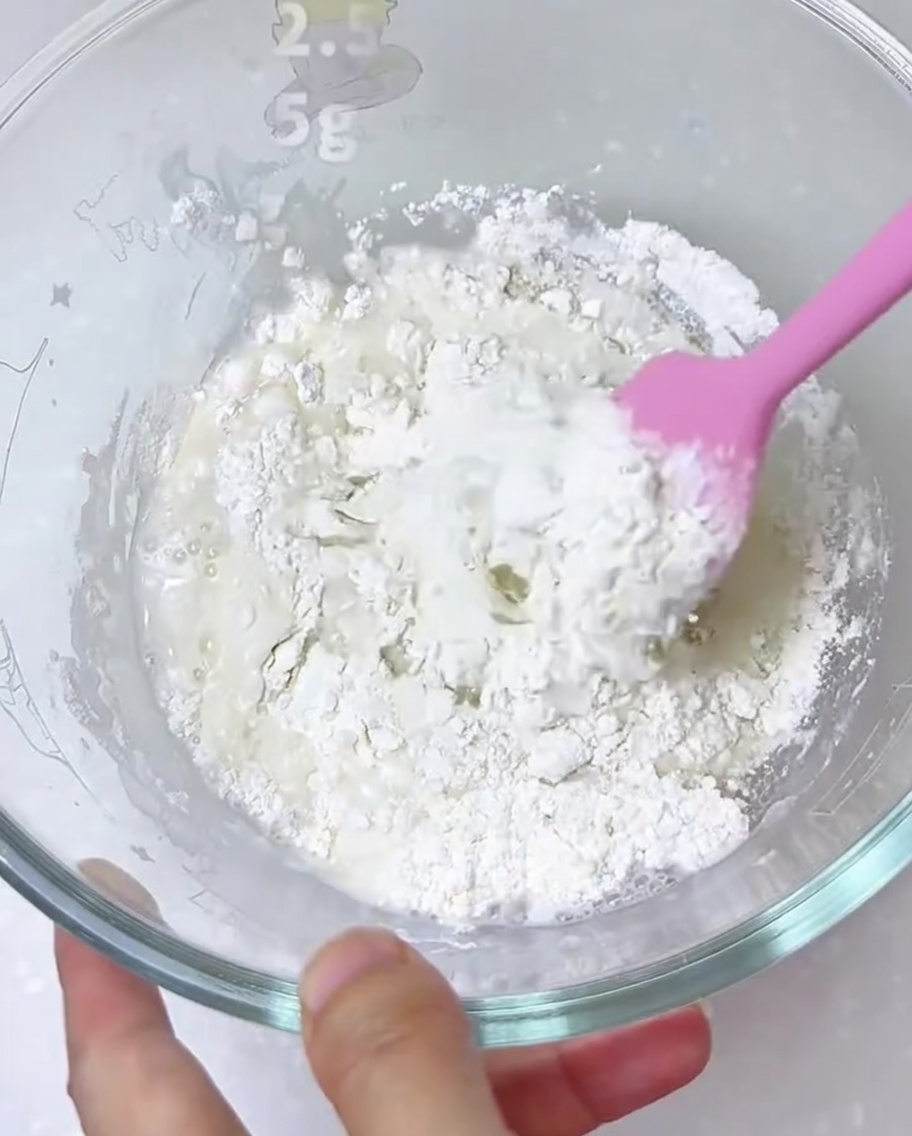 Ingredienti per limpasto della pizza mescolati in una ciotola di vetro con una spatola.