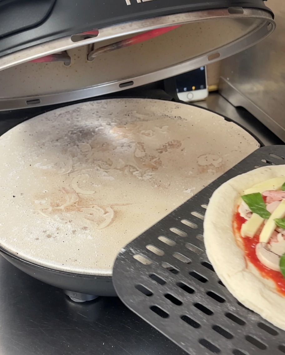 Impasto della pizza steso su una pietra refrattaria nera forata allinterno di un forno per pizza.