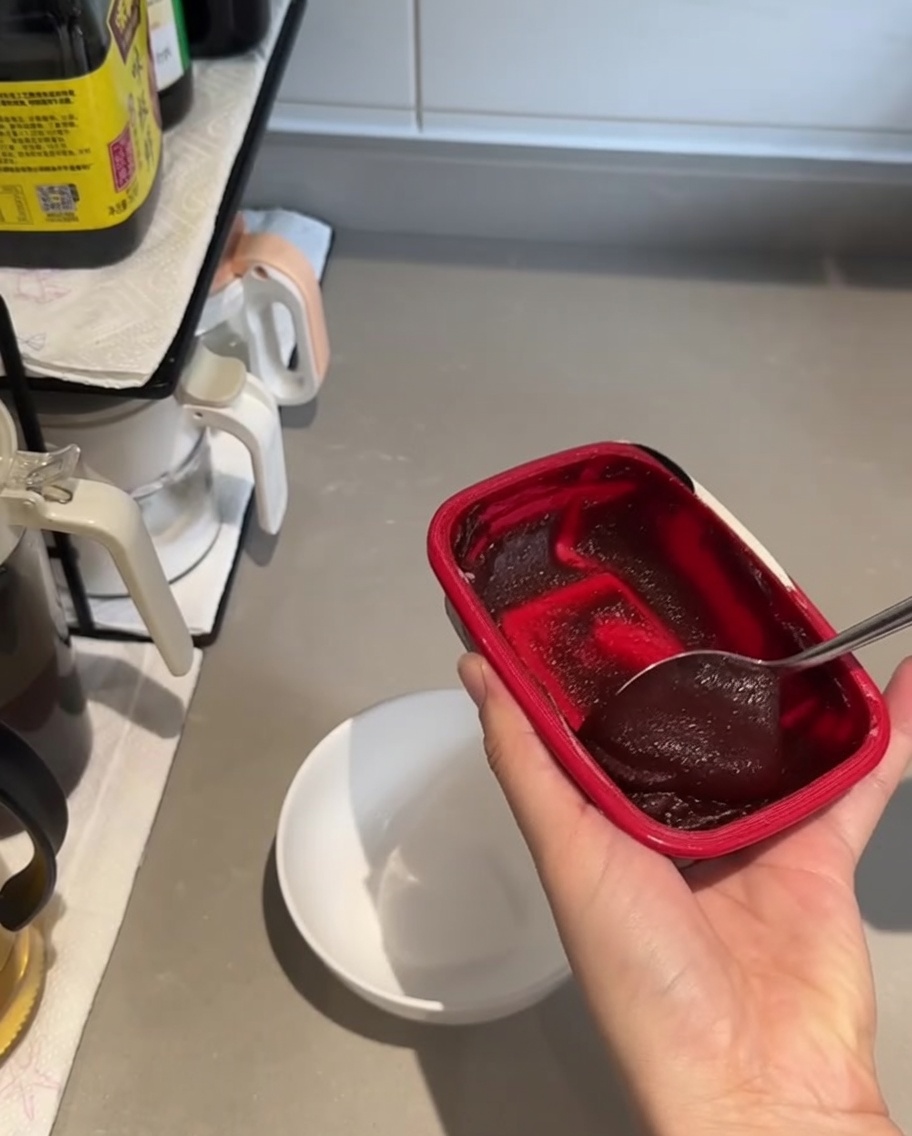 Una piccola ciotola bianca contenente un cucchiaio abbondante di pasta di gochujang rosso scuro e salsa di soia, pronta per essere mescolata.
