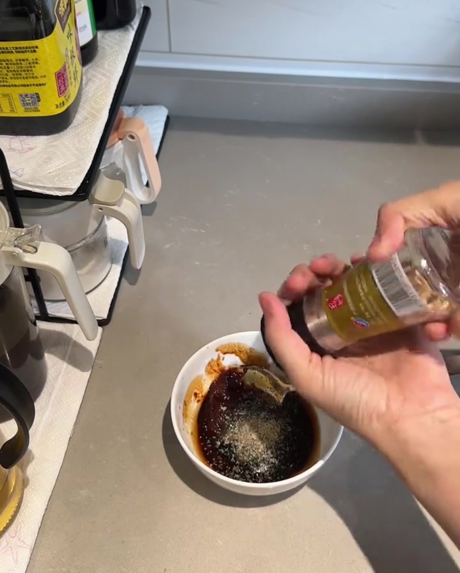 Un cucchiaio che mescola gli ingredienti densi e scuri della salsa in una piccola ciotola bianca.