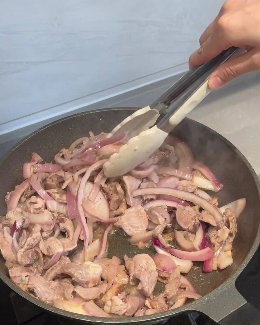 La salsa piccante viene versata sopra il maiale e le cipolle in una padella, con gli ingredienti mescolati insieme.