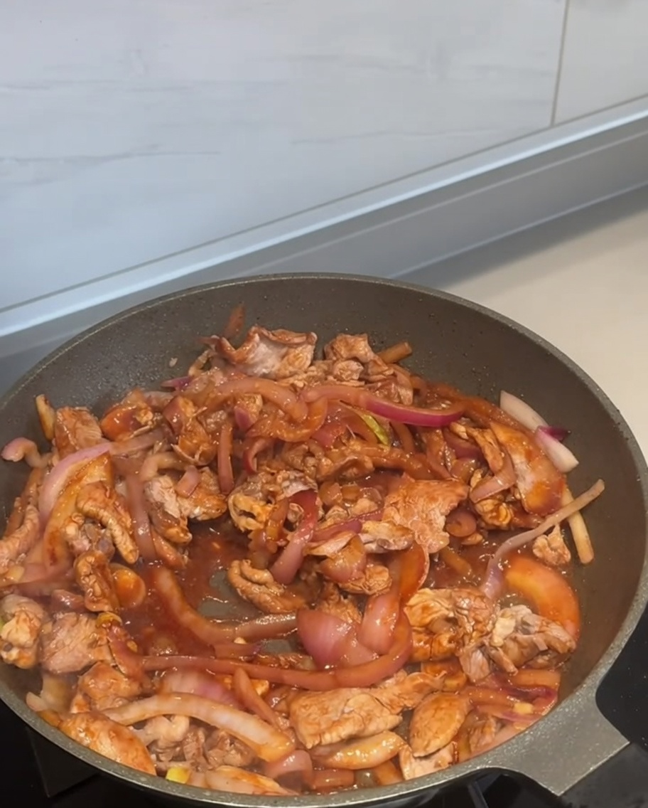 Peperoncino in polvere che viene cosparso sopra il maiale e le cipolle che soffriggono in padella.