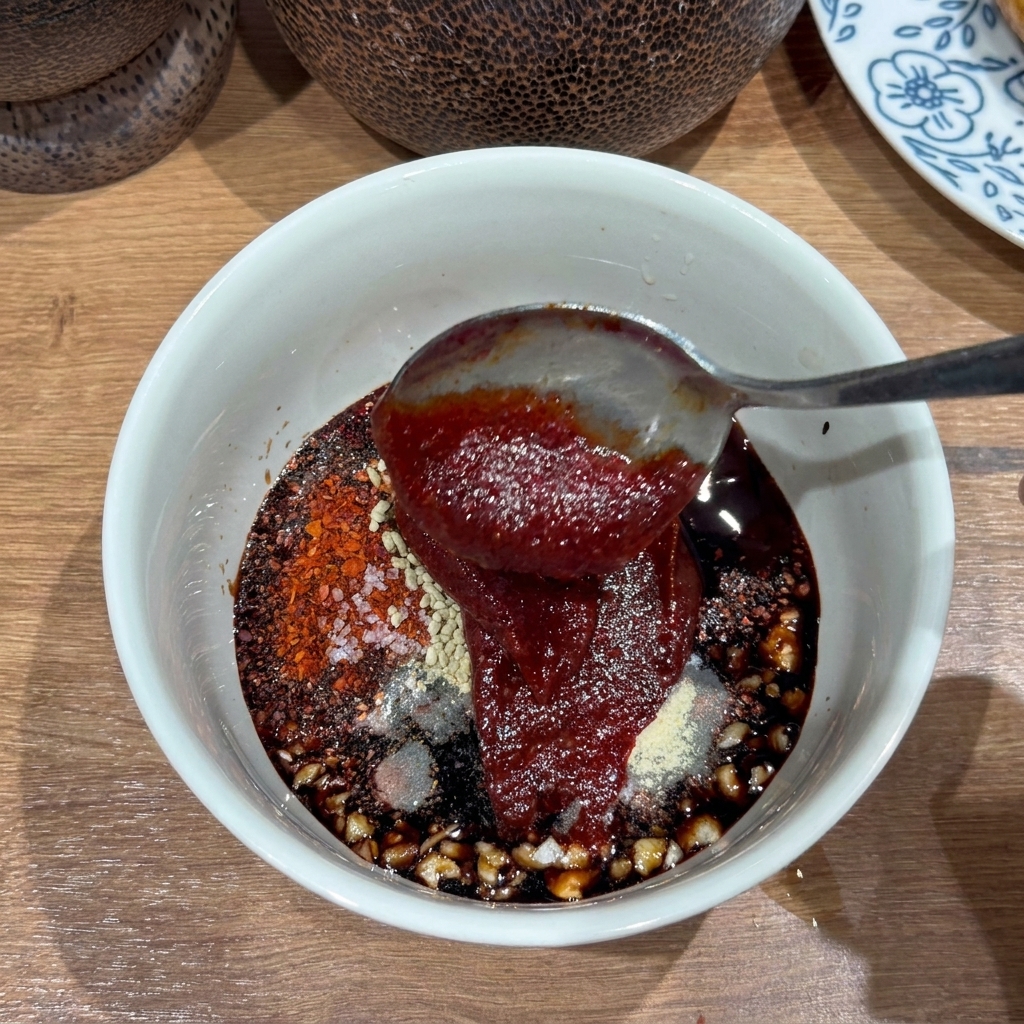 Primo piano di una ciotola bianca contenente una salsa densa e rosso scuro con aglio tritato e scaglie di peperoncino.