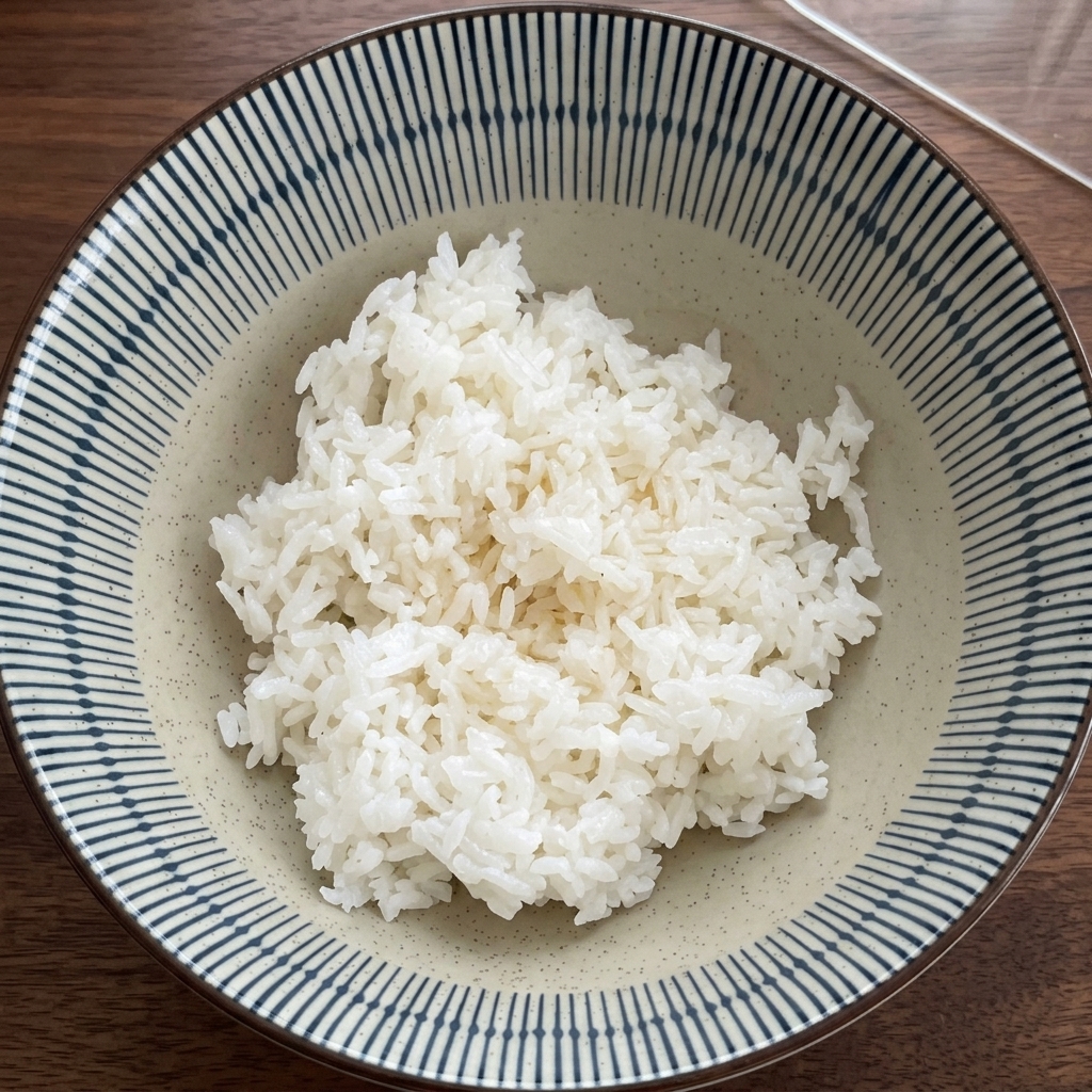 Una ciotola di riso bianco mescolato con alghe scure tritate da una mano con guanto in plastica.