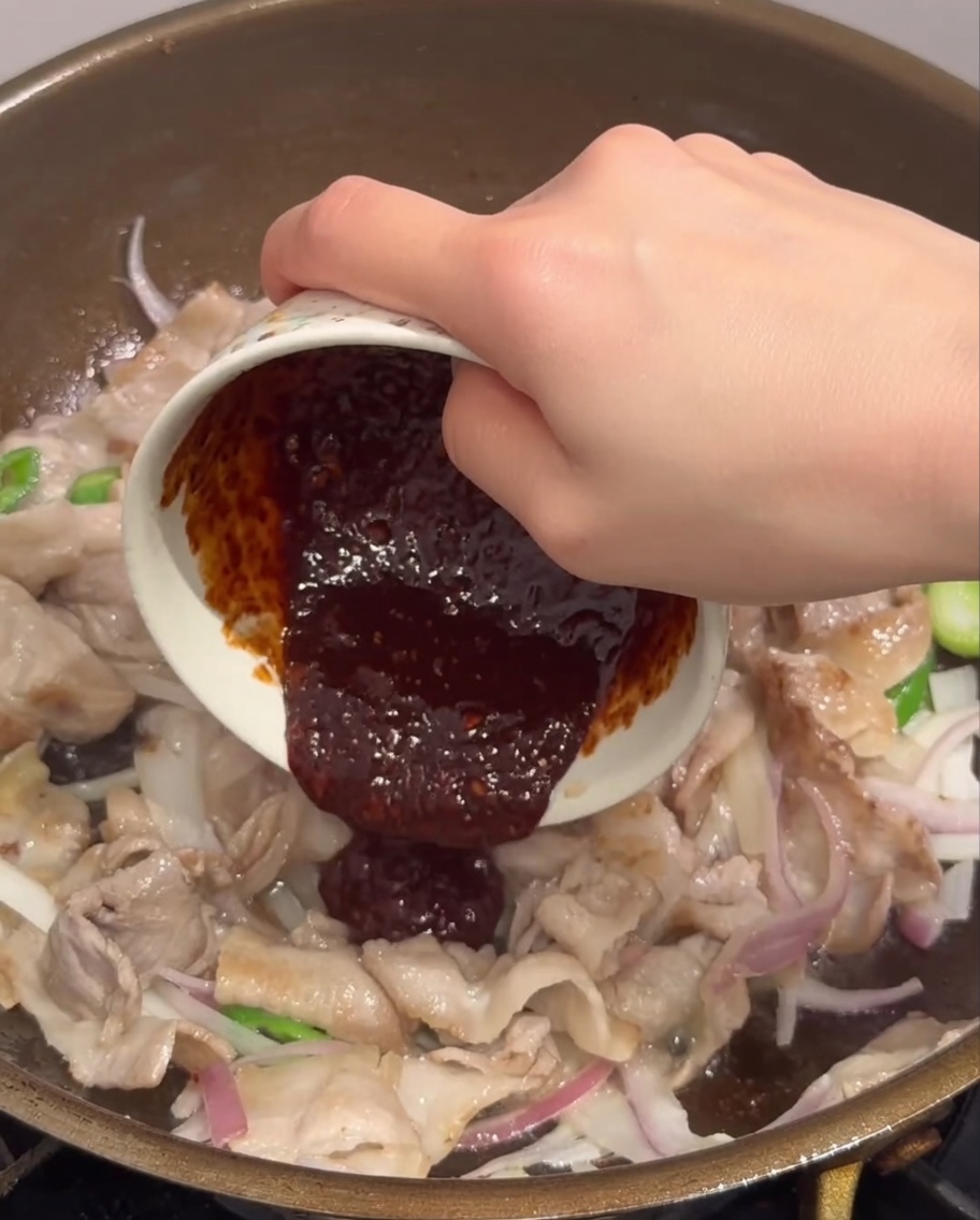 Salsa rosso scuro versata da una piccola ciotola in una padella piena di carne e verdure.
