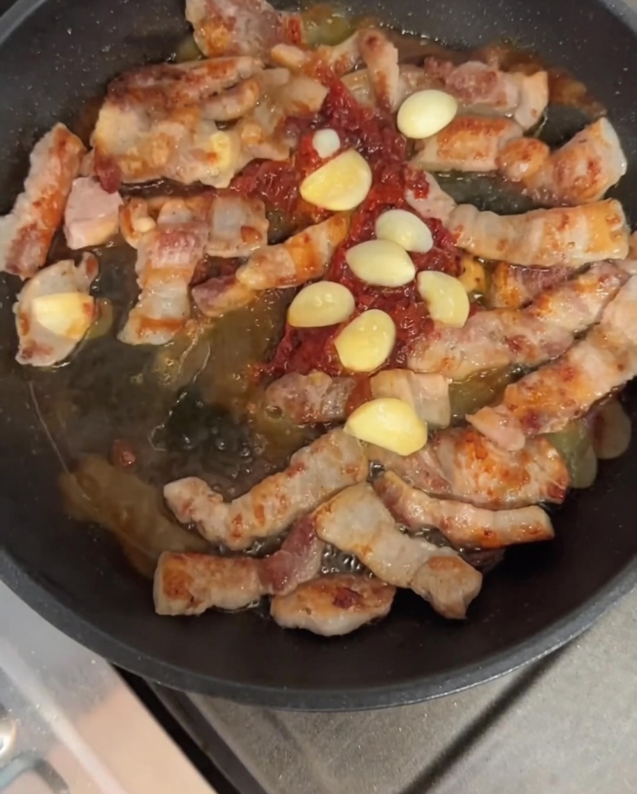 Pancetta e aglio saltati con la salsa nella padella.