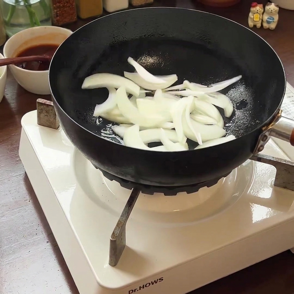 Cipolla affettata e kimchi in cottura in padella, che si ammorbidiscono con il calore.