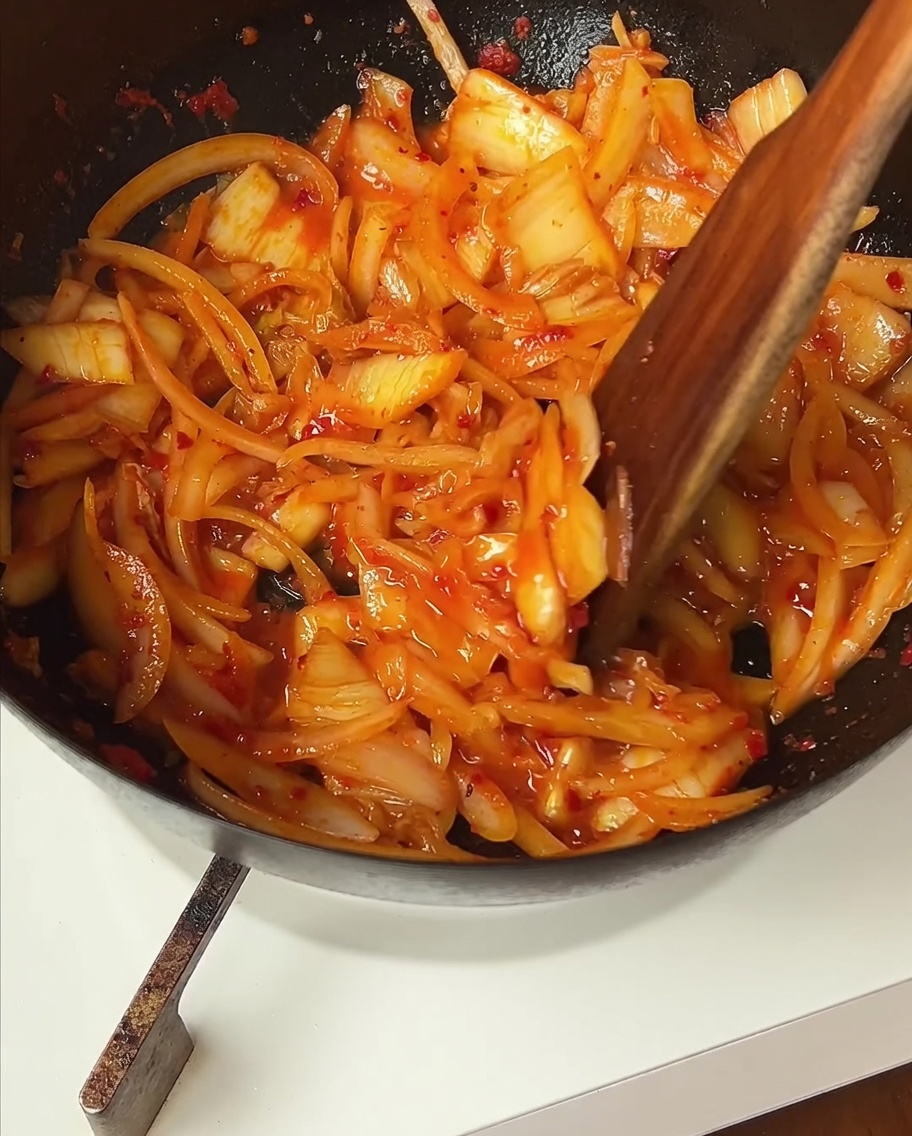 Il manzo rosolato viene aggiunto in padella con il kimchi e le cipolle saltate.