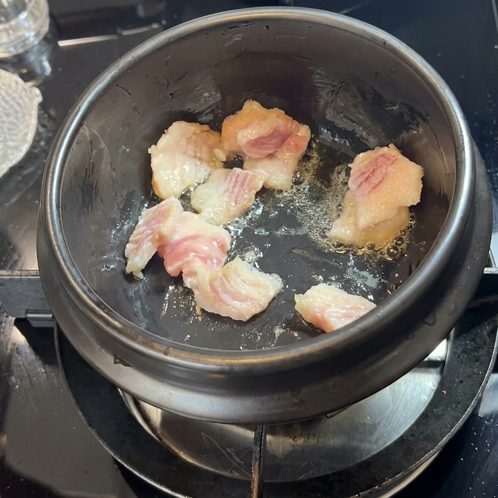Pezzi di pancetta che sfrigolano in un vaso di pietra nero.