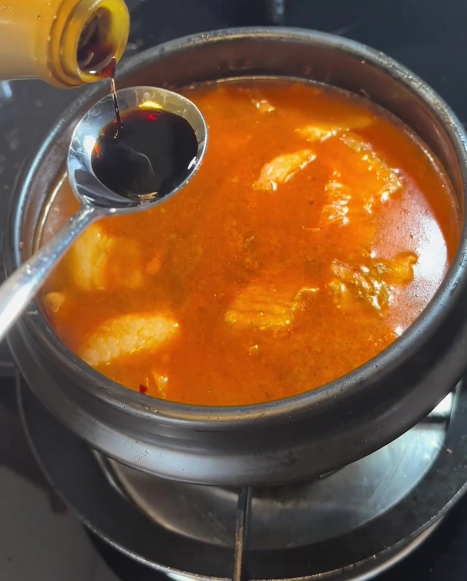 Un cucchiaio di salsa di soia aggiunto allo stufato bollente.