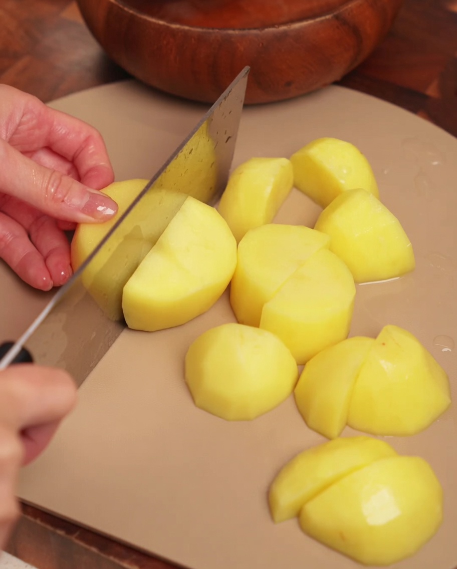 Patate pelate tagliate in grossi pezzi uniformi su un tagliere di legno.