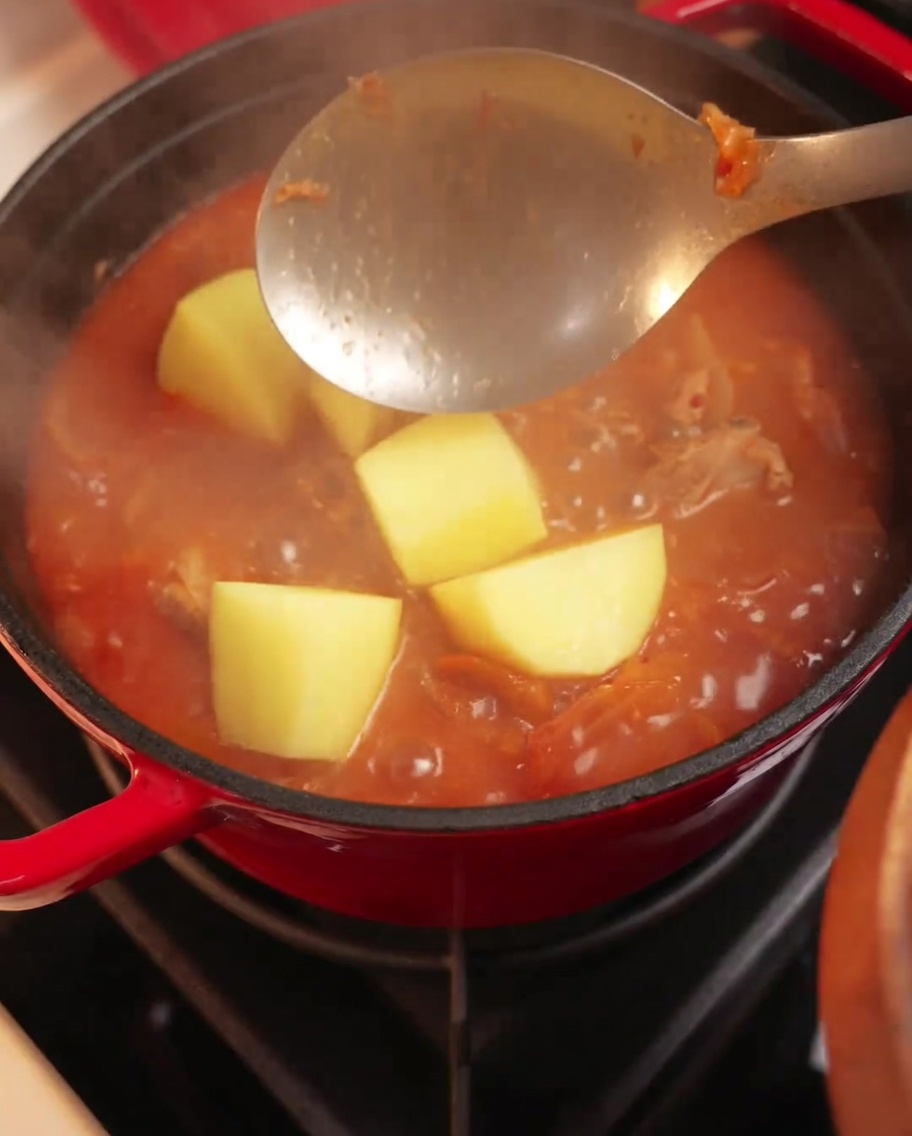 Cubetti di patate aggiunti in una pentola di stufato di maiale e kimchi in ebollizione.