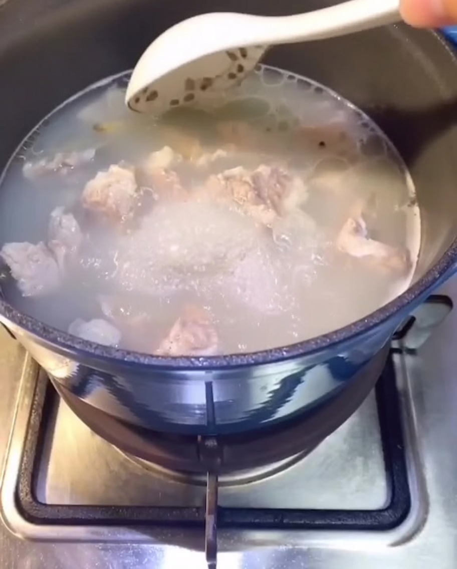 Costine di maiale che cuociono in una pentola dacqua sul fornello, si forma un brodo chiaro.