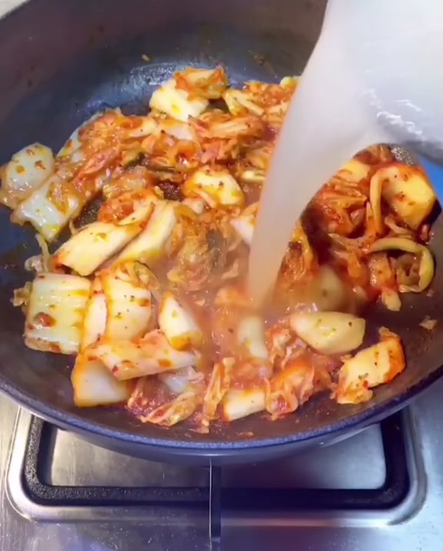 Brodo di costine di maiale versato nella padella contenente il kimchi soffritto.