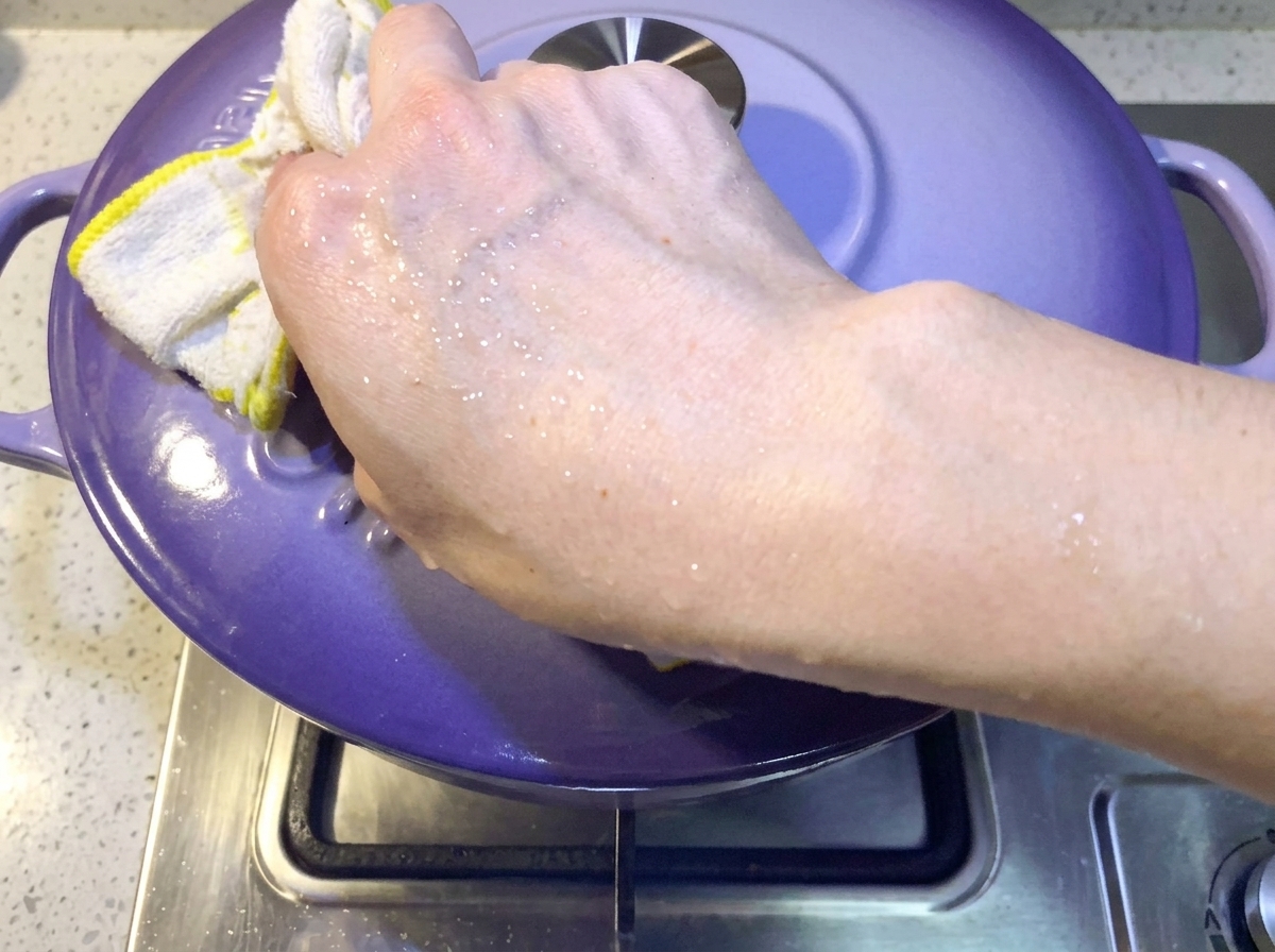 Mano che posiziona un coperchio viola sulla pentola per coprire lo stufato di kimchi e maiale.