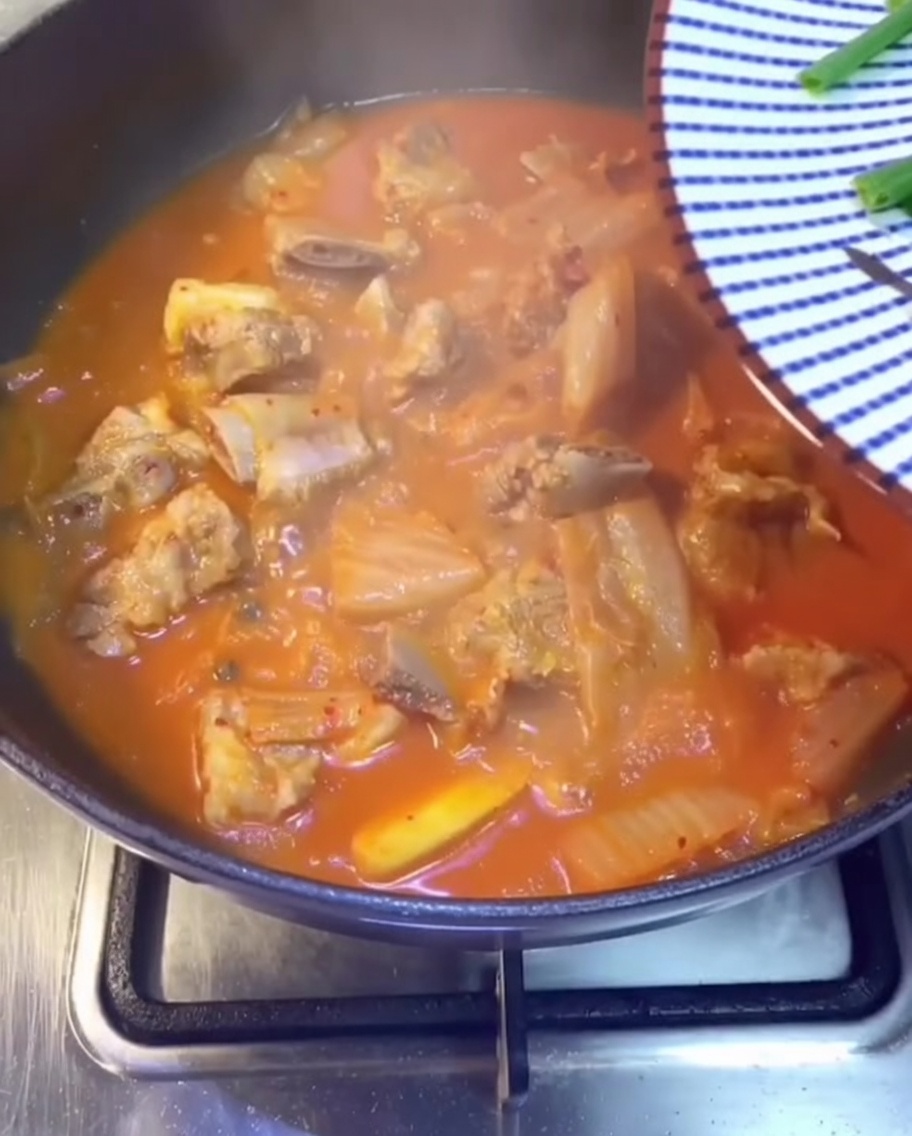 Primo piano di cipollotti freschi, coriandolo e peperoncini verdi affettati cosparsi sopra lo stufato rosso.