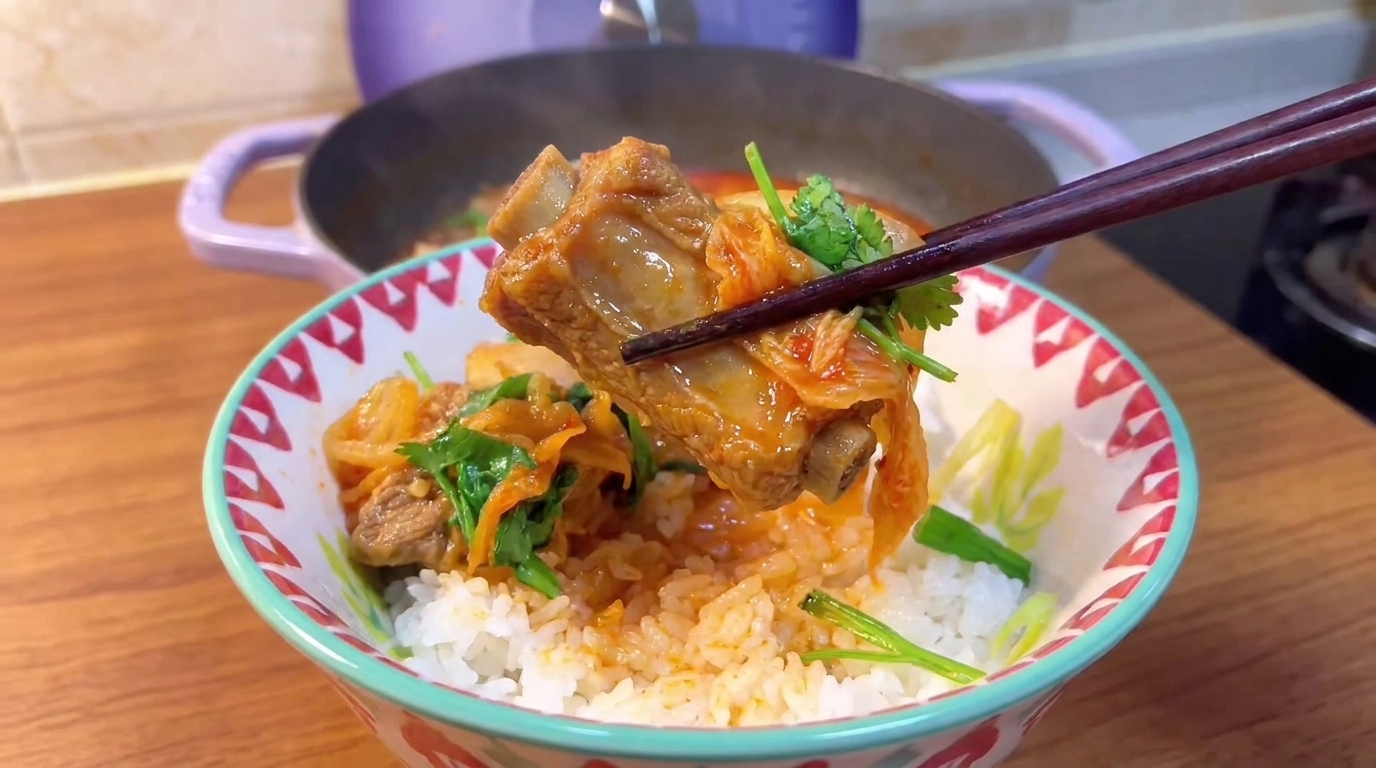 Una tenera costina di maiale e vivace kimchi sollevati con le bacchette sopra una ciotola di riso fumante.