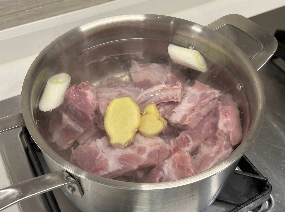 Pentola con costine di maiale, cipollotto, fette di zenzero e vino da cucina.