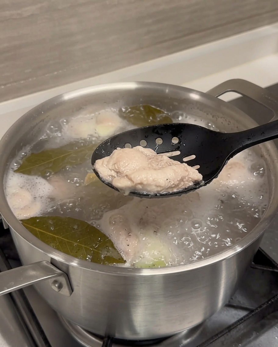 Una costina di maiale sbollentata sollevata dallacqua bollente con delle pinze nere.