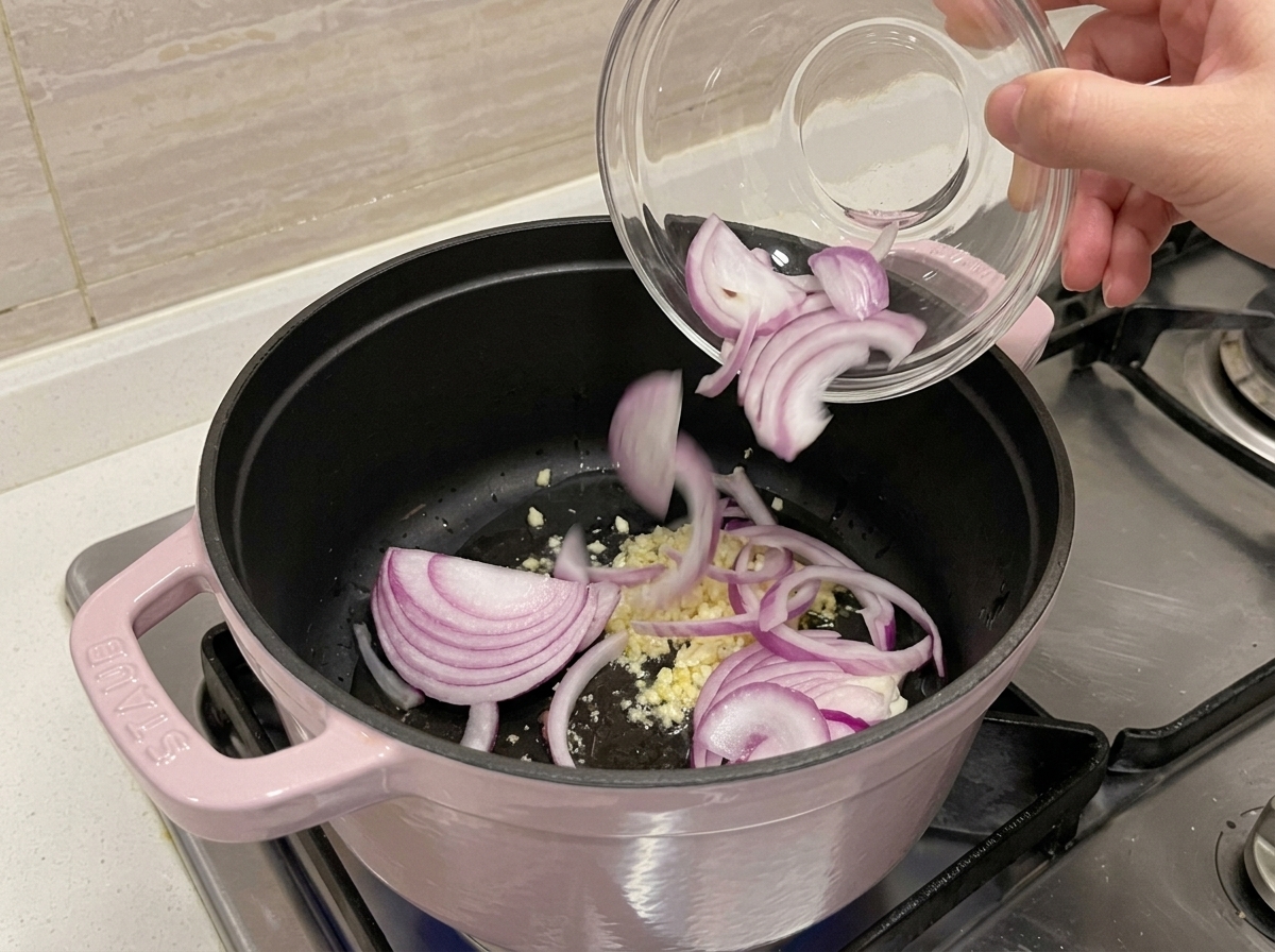 Aglio tritato e cipolla rossa affettata che soffriggono in una pentola con olio.