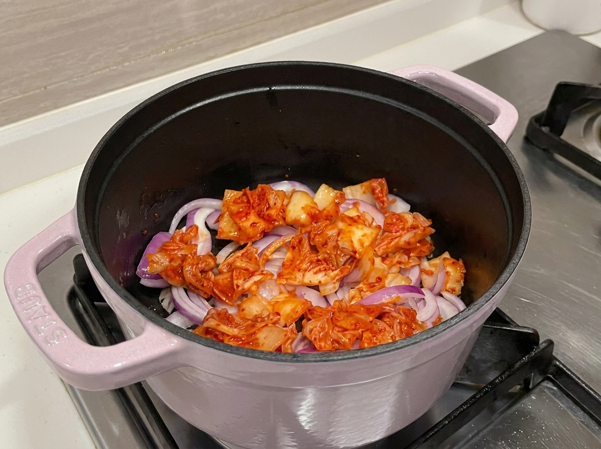Vista ravvicinata di kimchi rosso vibrante e cipolle che soffriggono in una pentola, rilasciando i loro succhi aromatici.
