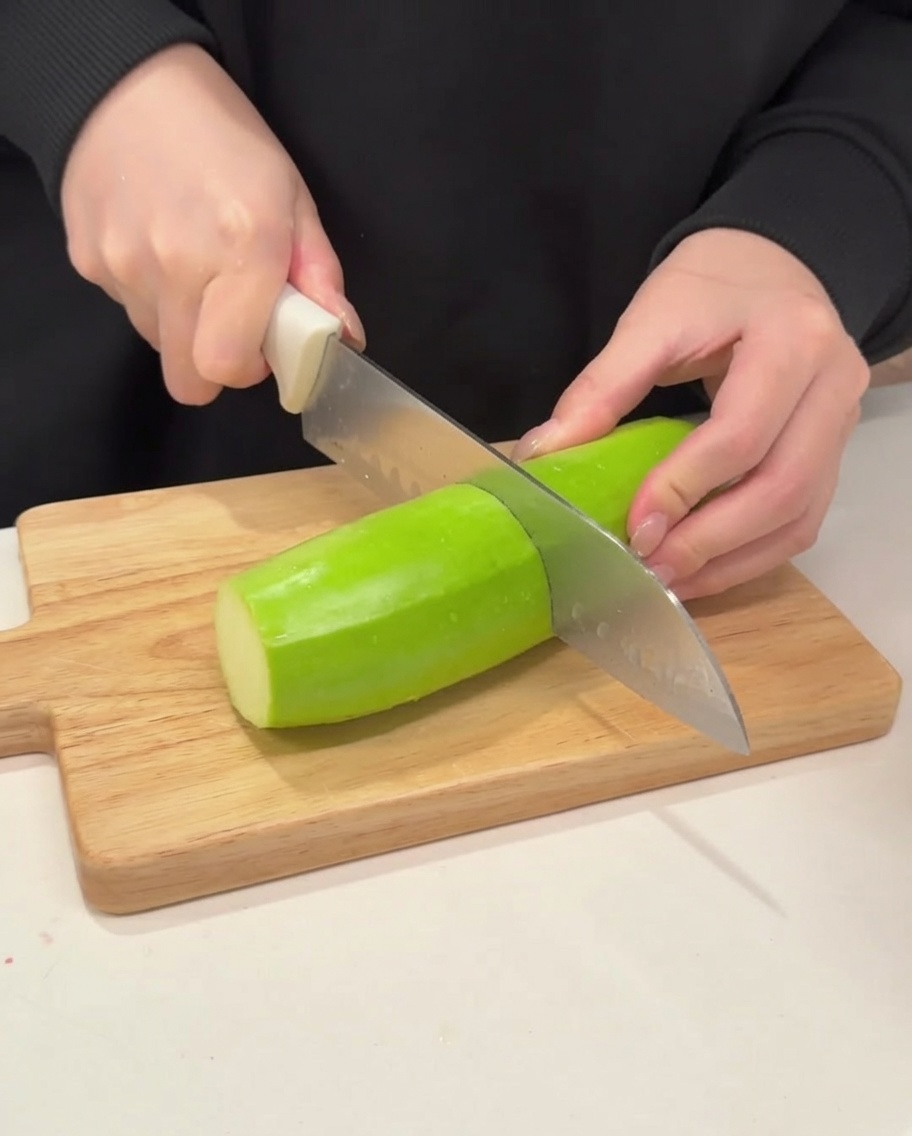 Un coltello affilato che affetta una zucchina verde soda e vibrante a semicerchi spessi su un tagliere di legno pulito.
