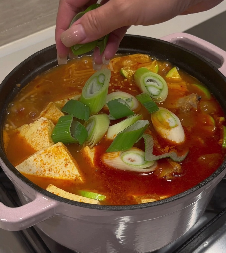 Cipollotti freschi affettati e peperoncini cosparsi su una pentola di zuppa di kimchi e costine di maiale finita.