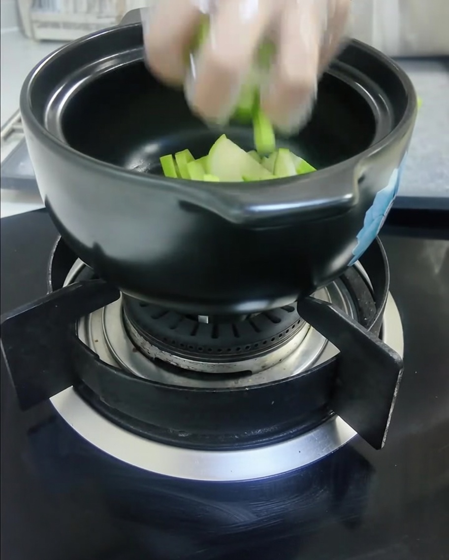 Zucchina verde affettata e cipolle bianche affettate sono messe in una pentola di ceramica nera.