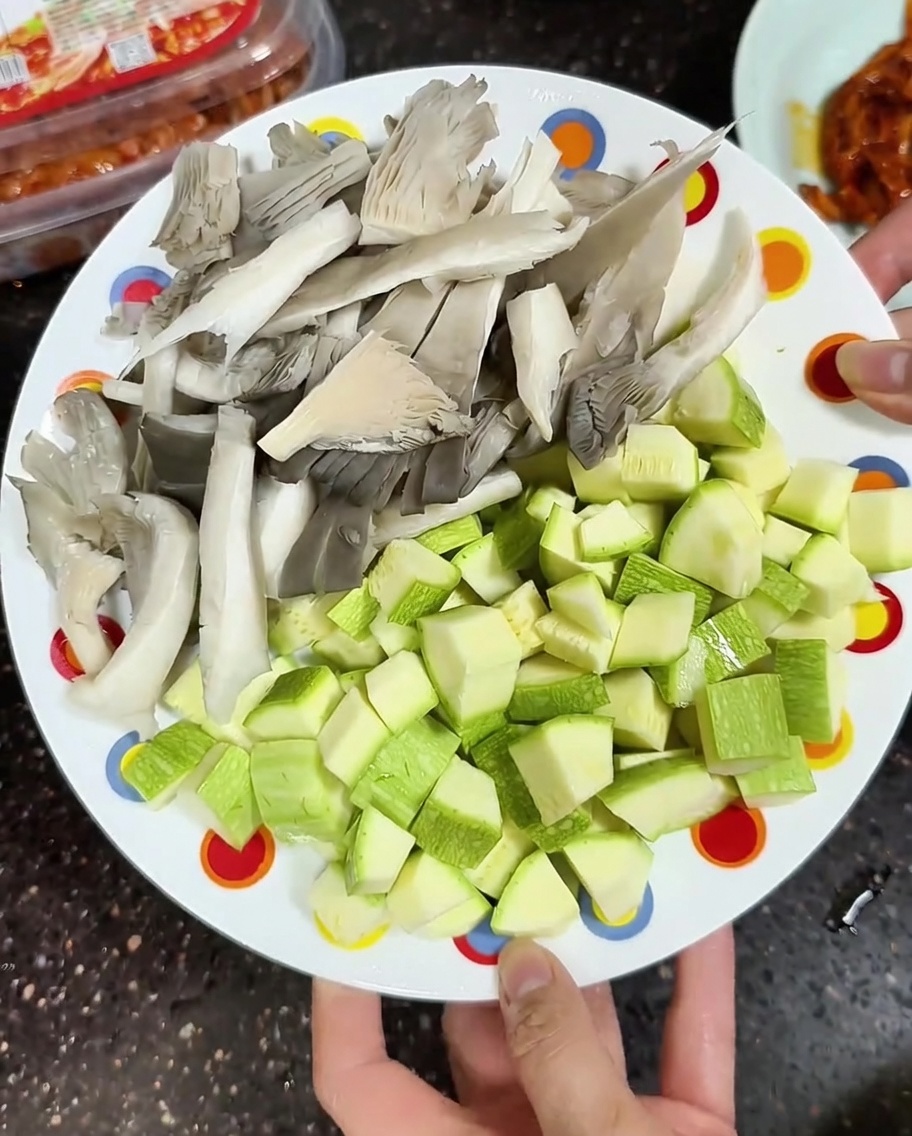 Un piatto con funghi ostrica affettati e zucchine a cubetti pronti per la cottura.