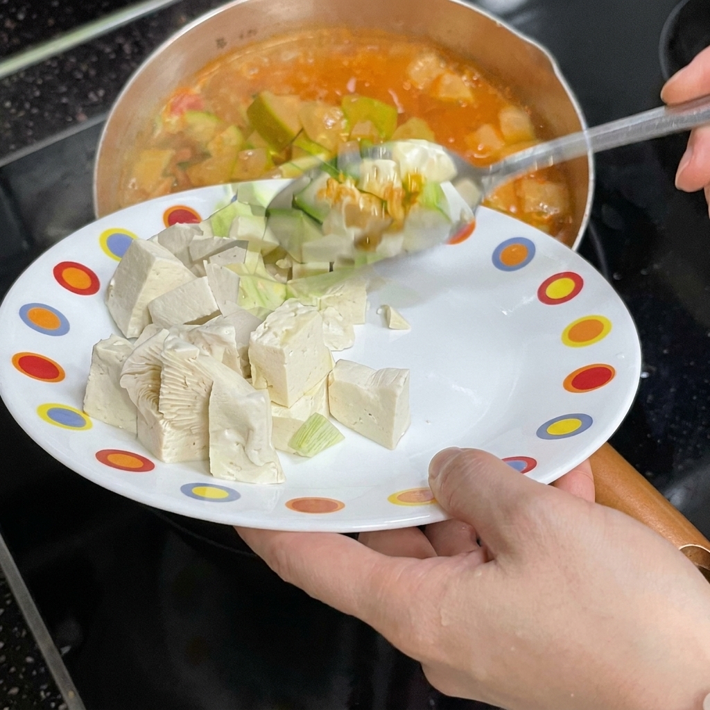 Cubetti di tofu bianco fatti scivolare da un piatto nel brodo bollente.