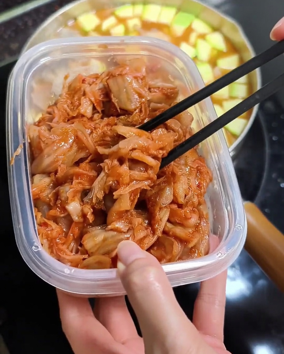 Bacchette che aggiungono kimchi rosso tritato allo stufato.