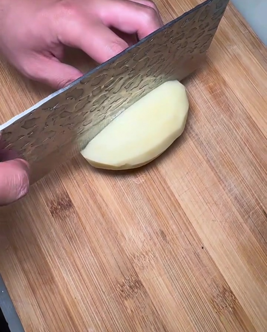 Fette di patata cruda su un tagliere di legno.