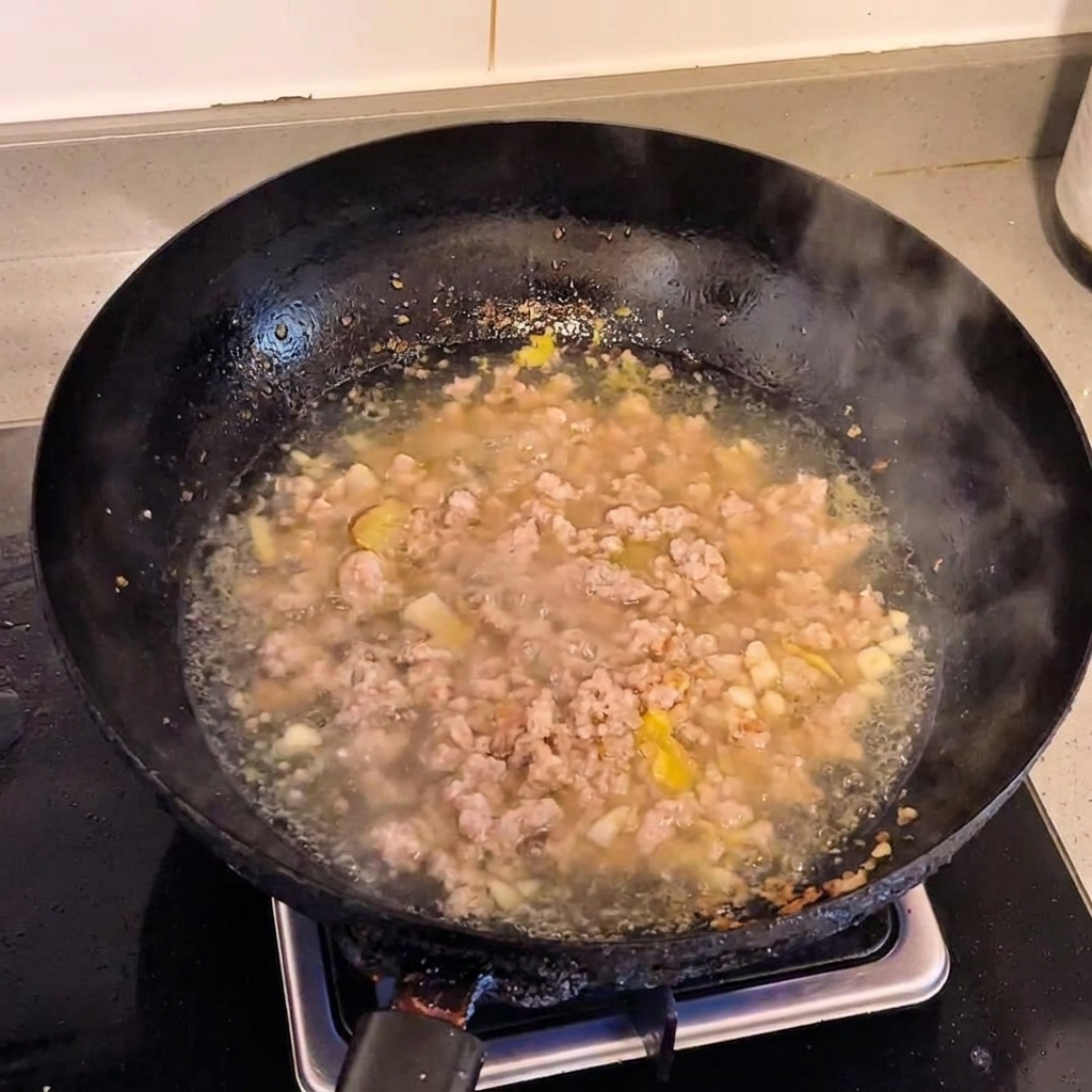 Una ciotola dacqua versata in un wok contenente maiale macinato cotto.