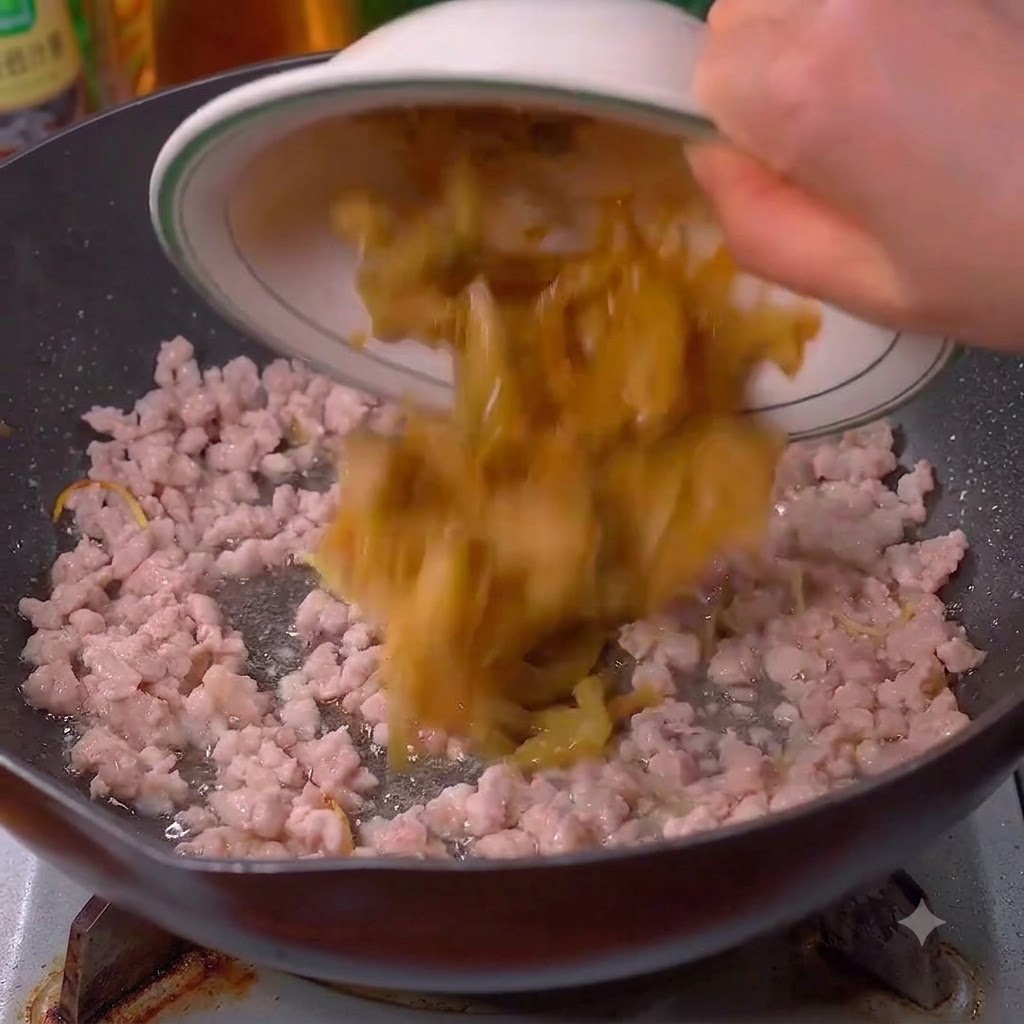 Senape sottaceto versata nel wok insieme alla carne di maiale.