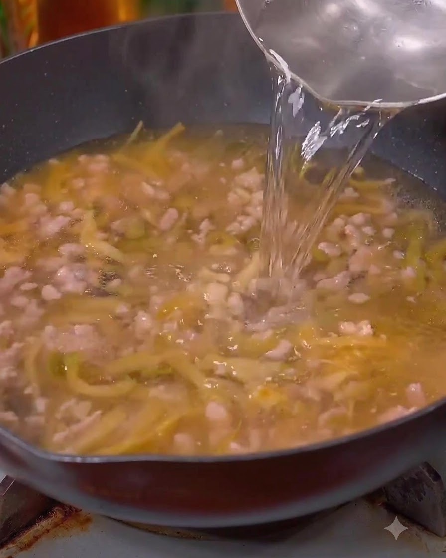 Acqua versata da una brocca nel wok sopra la carne e la senape.