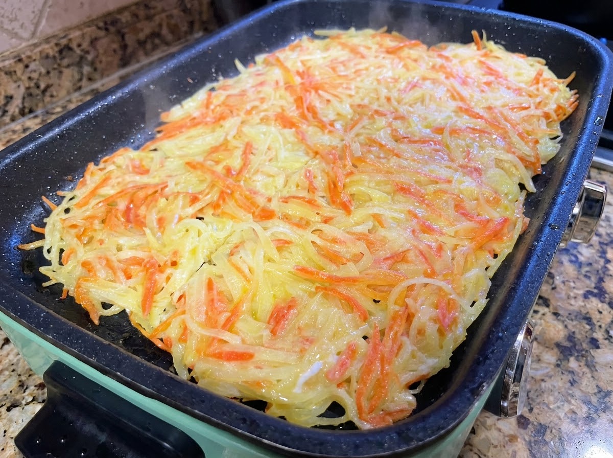 Una grande frittata di patate tagliata in porzioni più piccole con delle spatole da cucina in una padella.
