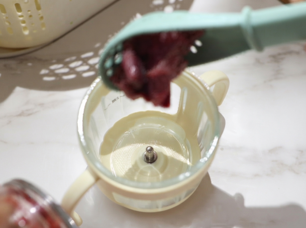 Pezzi di manzo crudo scolati e messi con un cucchiaio nella tazza di un piccolo robot da cucina per essere frullati.